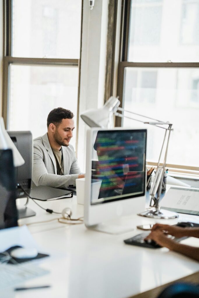 A young man working at a desktop computer in a bright, modern office environment.