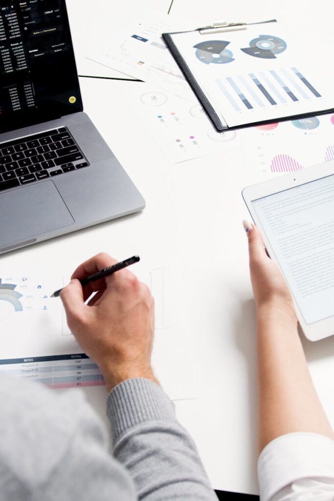 Two business professionals analyzing financial reports using a laptop and tablet in a modern office setting.
