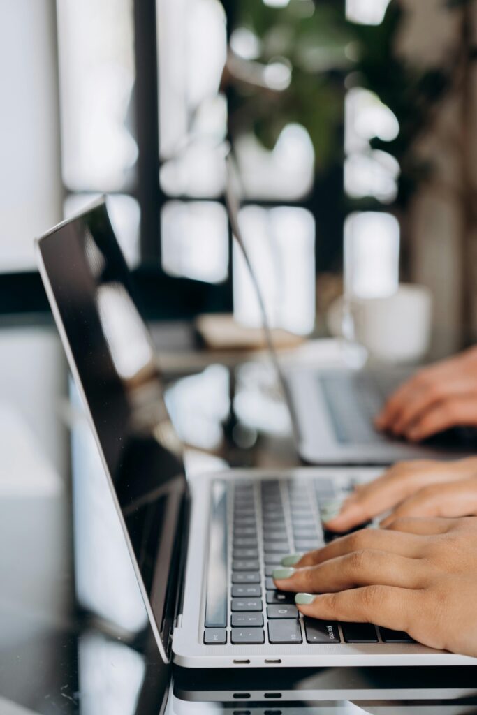 Close-up of hands typing on a sleek laptop keyboard in a bright, modern office setting.